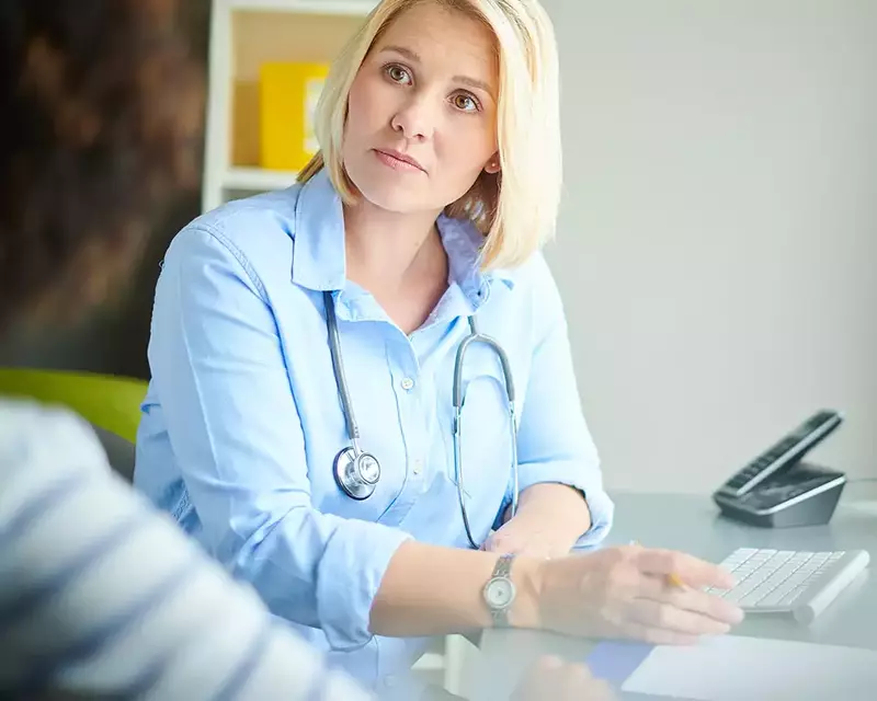 female doctor wearing stethoscope at desk with patient, appointment booked via hosted telephony system