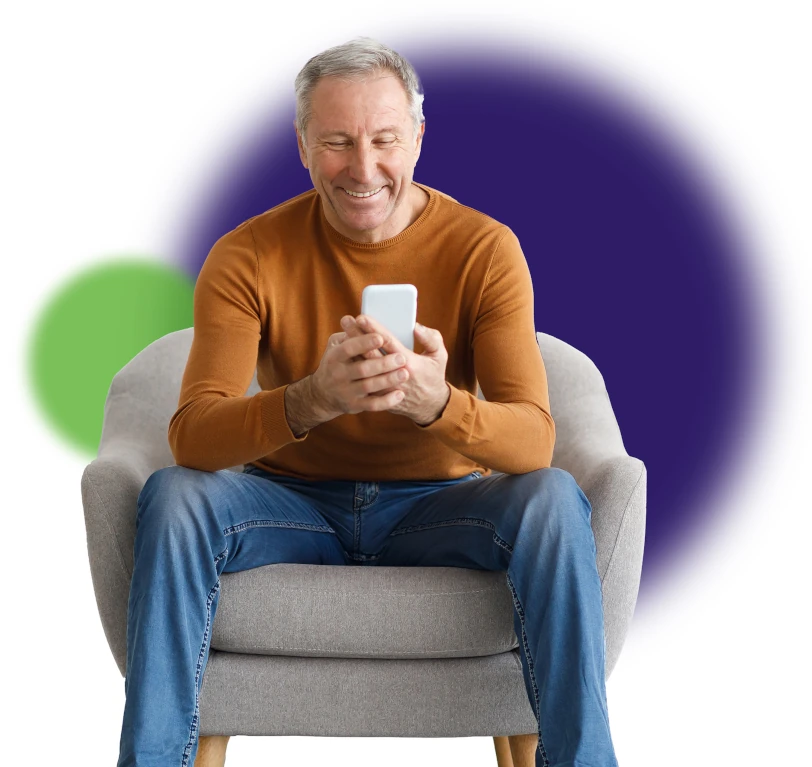 A man sitting in an armchair reading from a smartphone and smiling